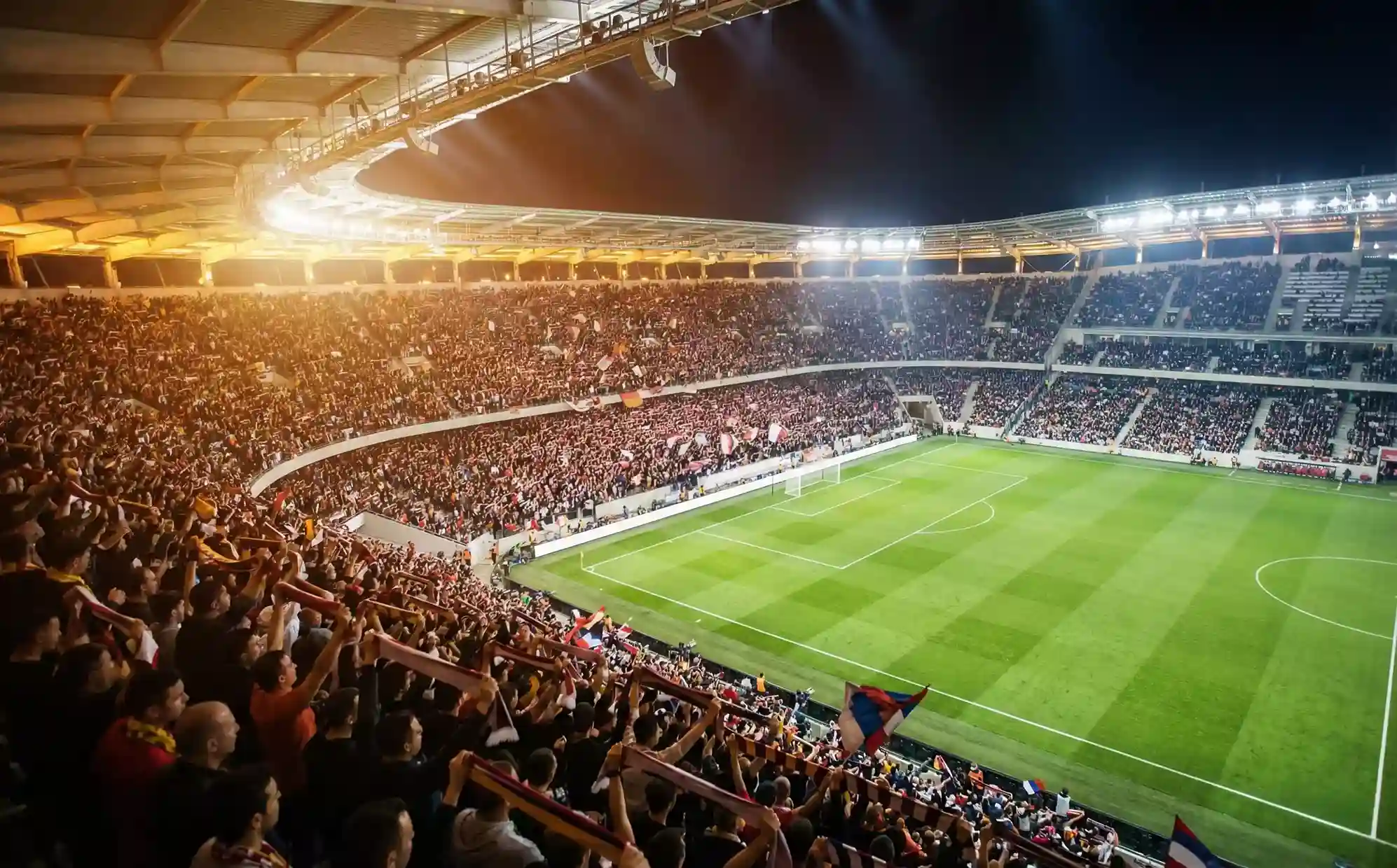 Stade de football illuminé lors d'un match de Ligue 1 avec supporters dans les tribunes